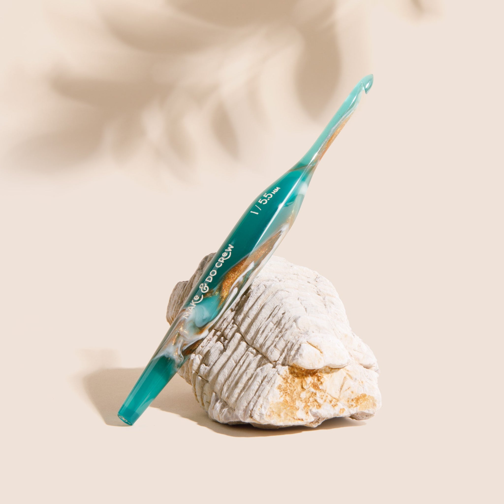 Teal ergonomic resin crochet hook on a rock with a beige background.