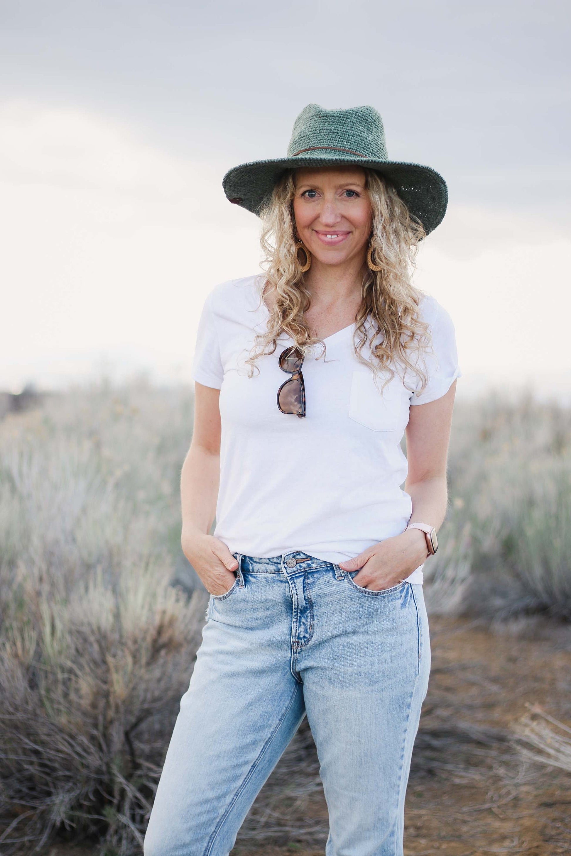 A person wearing a green Cleo Wide Brim Fedora Crochet Hat and a white t-shirt, standing in an outdoor setting.